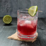 Side view of a pomegranate gimlet cocktail garnished with a lime wheel