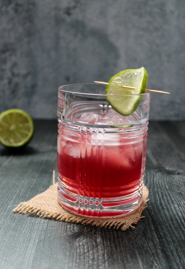 Side view of a pomegranate gimlet cocktail garnished with a lime wheel