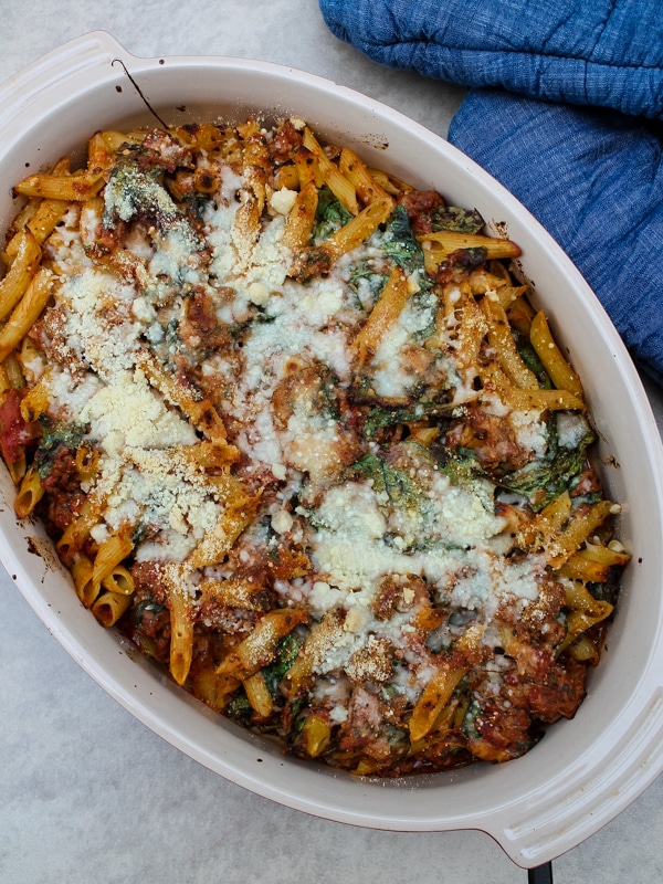 In this Baked Ziti with Sausage & Spinach, spicy Italian sausage, fresh spinach, and a tomato-pesto sauce are tossed with penne or ziti noodles for a flavorful, unique spin on the classic baked ziti recipe. Comfort food at its finest.