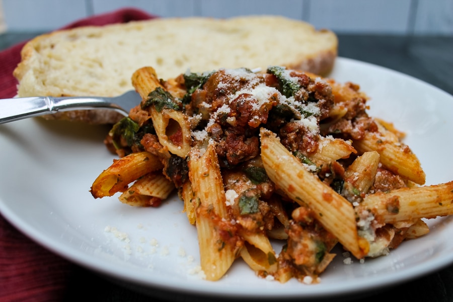In this Baked Ziti with Sausage & Spinach, spicy Italian sausage, fresh spinach, and a tomato-pesto sauce are tossed with penne or ziti noodles for a flavorful, unique spin on the classic baked ziti recipe. Comfort food at its finest.