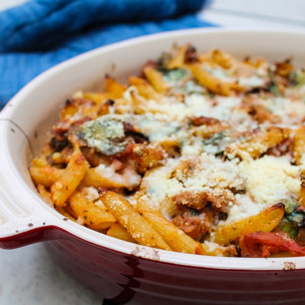 In this Baked Ziti with Sausage & Spinach, spicy Italian sausage, fresh spinach, and a tomato-pesto sauce are tossed with penne or ziti noodles for a flavorful, unique spin on the classic baked ziti recipe. Comfort food at its finest.