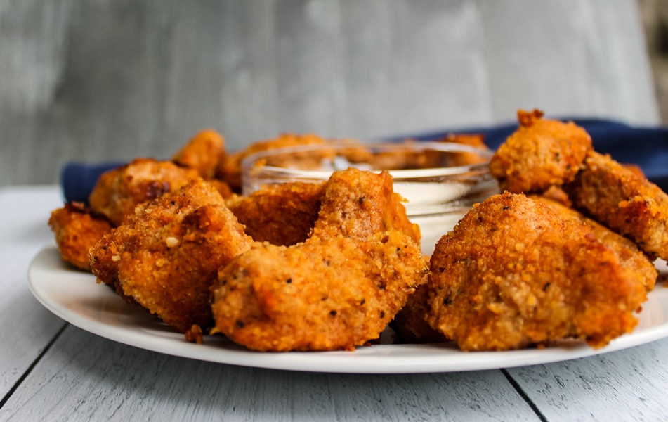 Side view of a plate of baked buffalo chicken nuggets with a bowl of blue cheese dressing in the center for dipping.