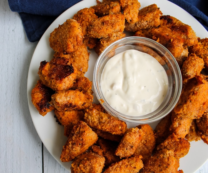 Overhead view of a plate of baked buffalo chicken nuggets with a bowl of blue cheese dressing in the center for dipping.