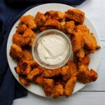 Overhead view of a plate of baked buffalo chicken nuggets with a bowl of blue cheese dressing in the center for dipping.