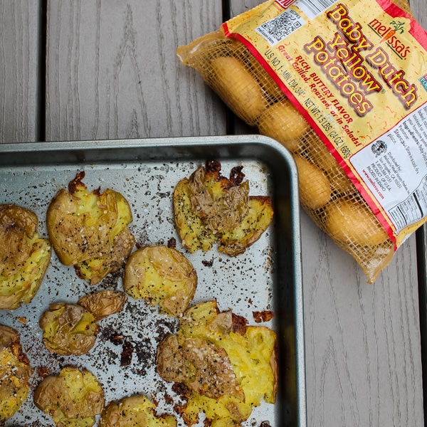 Corner of a baking sheet with crispy smashed dutch potatoes straight from the oven, next to a bag of the uncooked potaotes