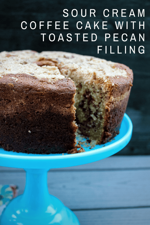 Side view of sour cream coffee cake with toasted pecan filling, set on a blue cake stand. Cake has a slice taken out of it, showing off the pecan swirl