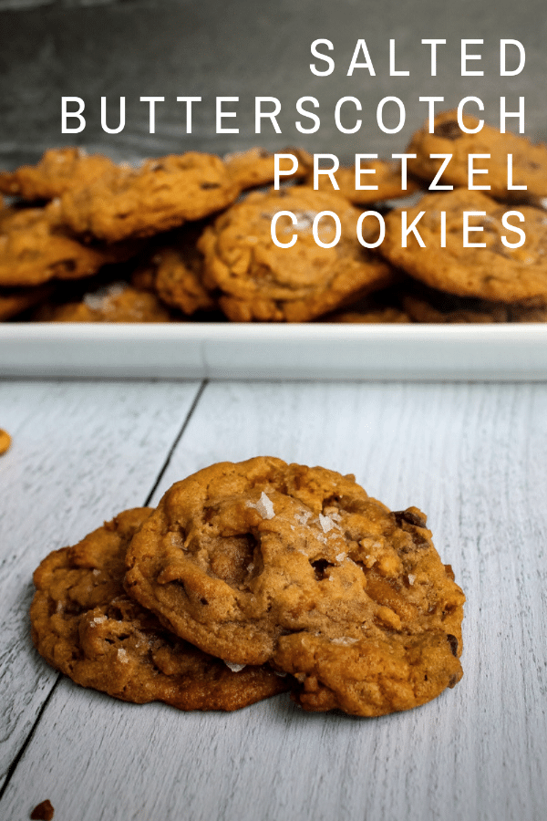 Pin of Salted Butterscotch Pretzel Cookies on Books n' Cooks - Salted Butterscotch Pretzel Cookies piled on a white plate in the background with two cookies in the foreground, against a white background.