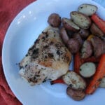 Overhead shot of roasted chicken thigh, potatoes and carrots in a white bowl, with an orange background