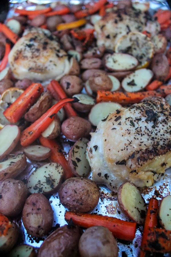 Overhead view of roasted chicken thighs, potatoes and carrots on a foil-covered sheet pan.