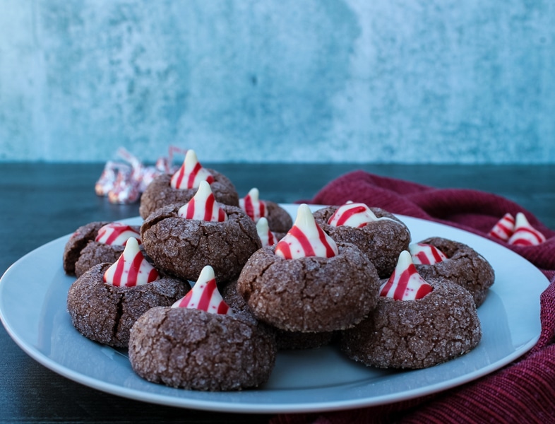 side view of chocolate cookies with a candy cane kiss on a white plate