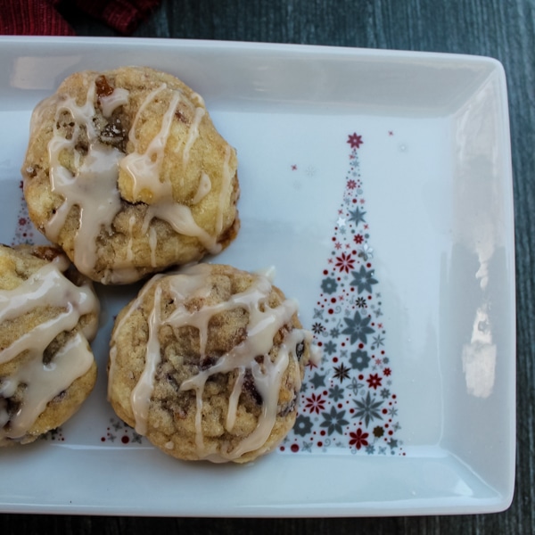 Overhead view of 3 fruitcake cookies with rum glaze on a white plate with a silver and red Christmas tree on the right.