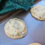 two honey walnut cookies on a baking sheet, with a corner of green and gold cloth slipping onto a corner of the baking sheet