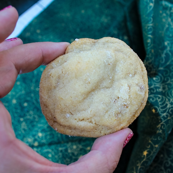 thumb and index finger holding a single honey walnut cookie, set on a green and gold cloth background