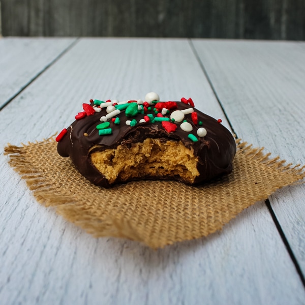 side view of a chocolate covered peanut butter cookie set on a piece of brown burlap on a white background