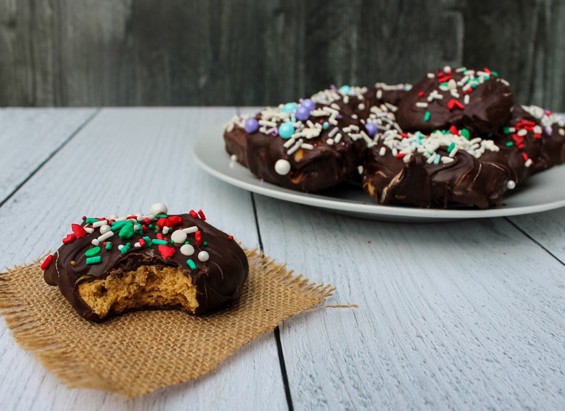 Side View: a chocolate peanut butter cookie with a bite taken out of it in the foreground, left, with a plate of cookies in the background, right. 