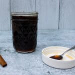 side view of a mason jar of Brown Sugar Cinnamon Simple Syrup, with a white lid and spoon