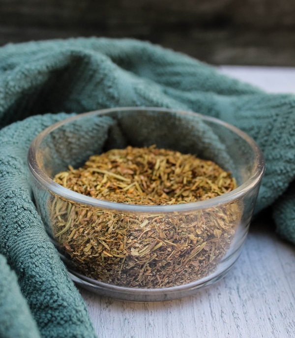 Side view of a clear bowl of Greek Seasoning Spice Blend set against a green and white background