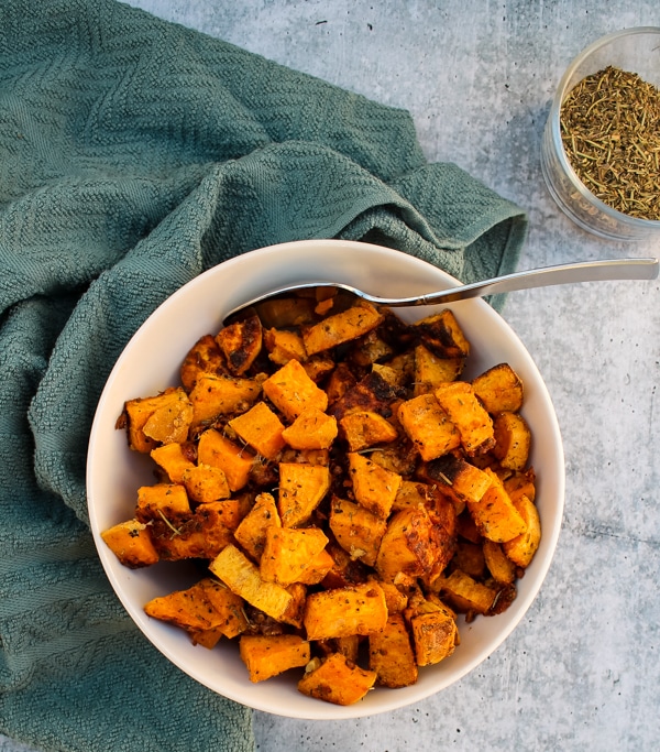 overhead view of Parmesan & Garlic Roasted Sweet Potatoes in a white bowl, with a small clear bowl of Green Seasoning in the top right corner