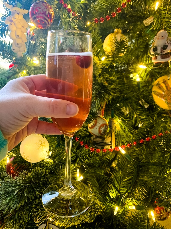 side view of Poinsettia Champagne Cocktail in front of a Christmas tree