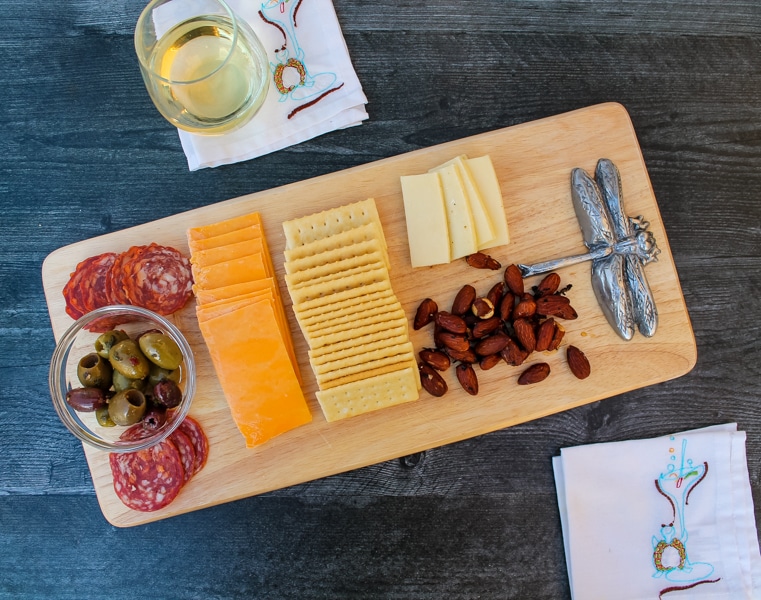 overhead view of a cheese board filled with salami, cheese, crackers, olives, and honey & rosemary almonds