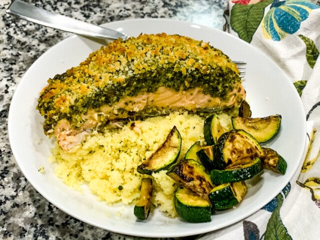 overhead view of pesto crusted salmon in a white bowl with couscous and zucchini