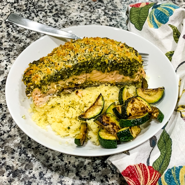 overhead view of pesto crusted salmon in a white bowl with couscous and zucchini