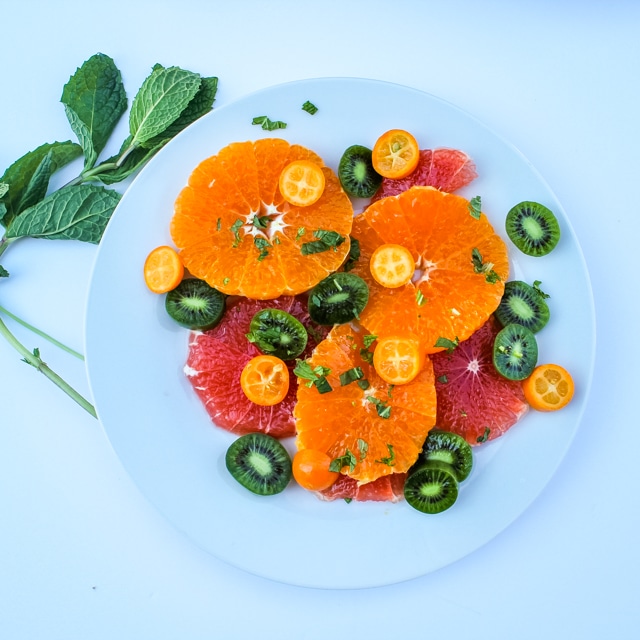 overhead view of citrus & mint fruit salad on a white plate