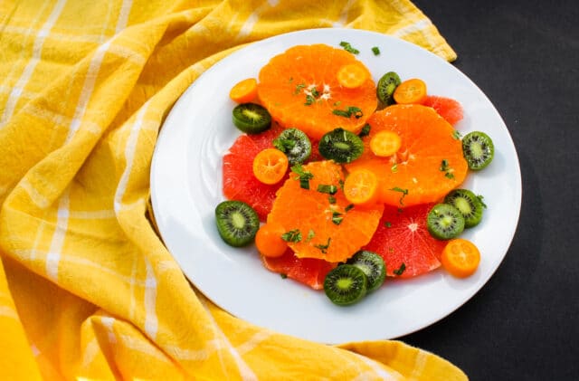 overhead view of citrus & mint fruit salad on a white plate