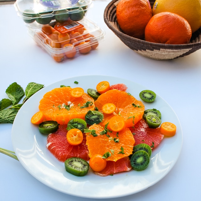 Citrus & Mint Fruit Salad on a white plate with extra fruit in the background