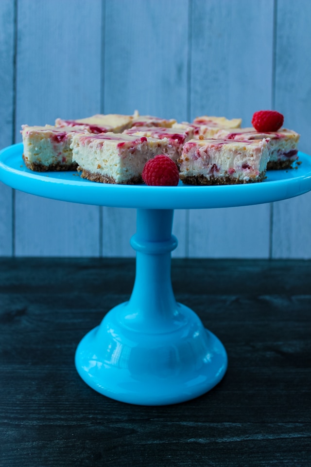 side view of Raspberry Cheesecake Bars on a blue pedestal cake stand