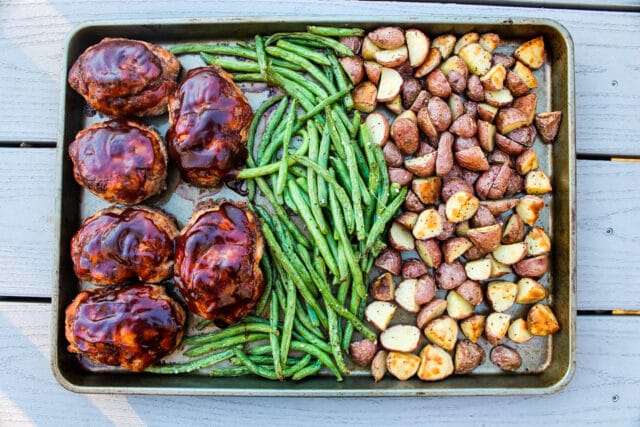 overhead view of individual BBQ meatloaves, green beans and roasted potatoes on a sheet pan