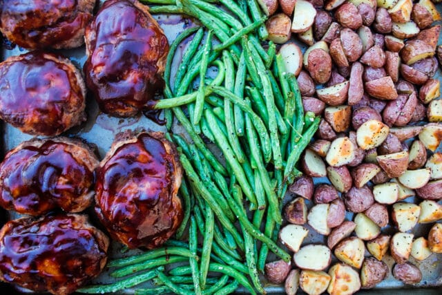 overhead view of individual BBQ meatloaves, green beans and roasted potatoes on a sheet pan