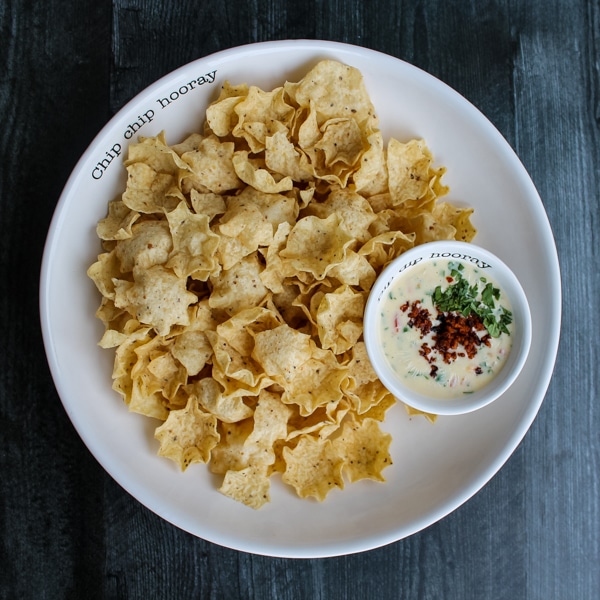 overhead view of queso topped with crumbled chorizo, amongst a large white serving bowl of tortilla chips