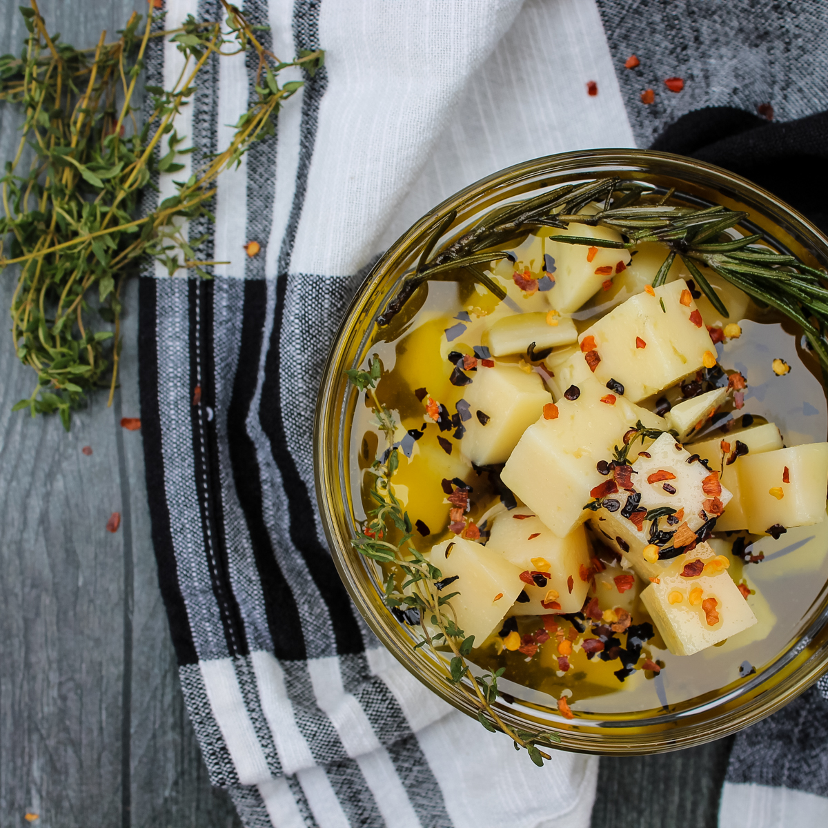 overhead view of Manchego Marinated in Olive Oil & Herbs in clear bowl