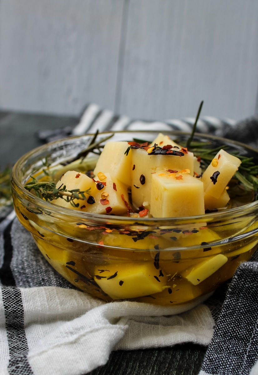 side view of Manchego Marinated in Olive Oil & Herbs in a clear bowl