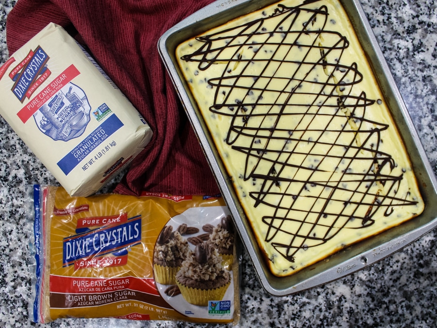 overhead view of a tray of Chocolate Chip Cheesecake Bars (uncut) with bags of dixie crystals sugar