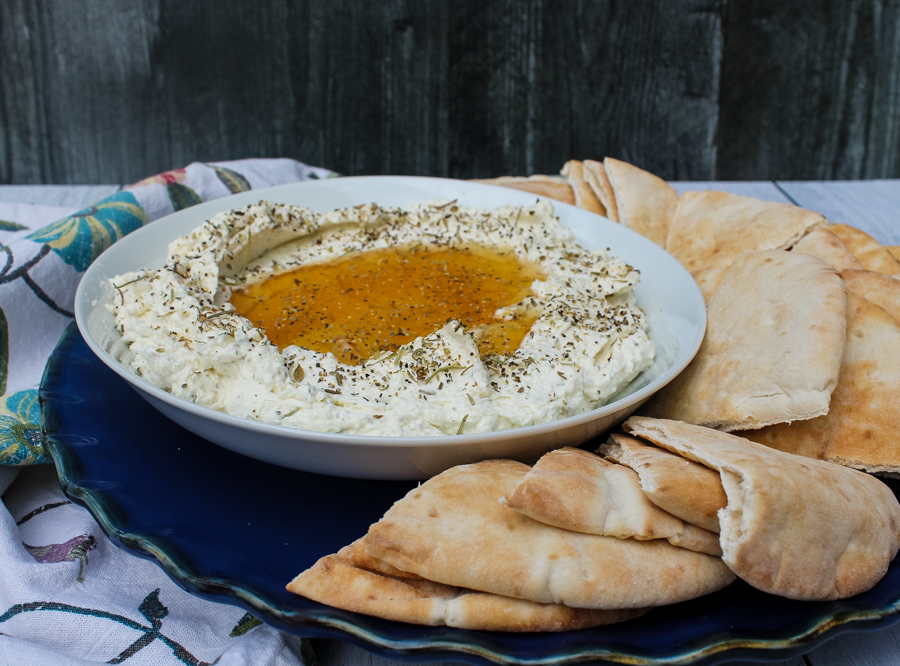 side view of Whipped Feta with Honey on a white plate, surrounded by pita slices